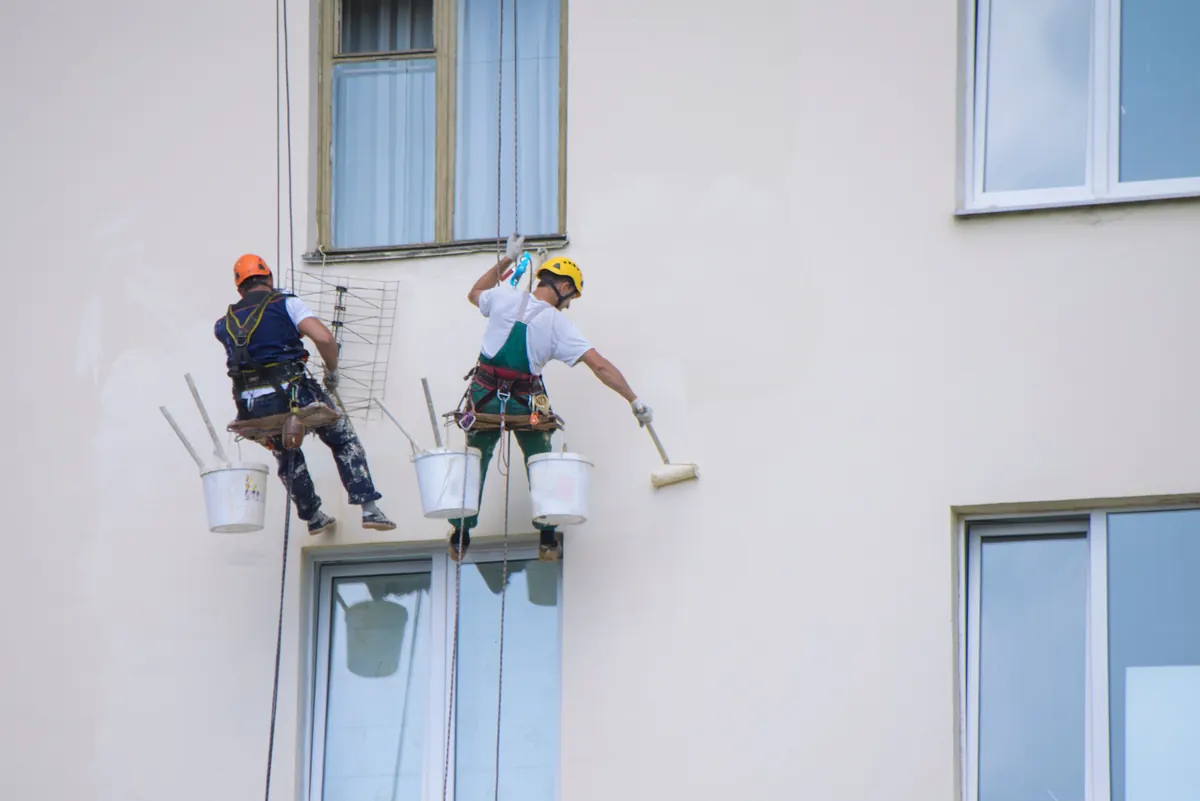 Painters on ropes rolling paint onto a multi-story building exterior, commercial painting by Blue Oak Painting Company in Houston, TX