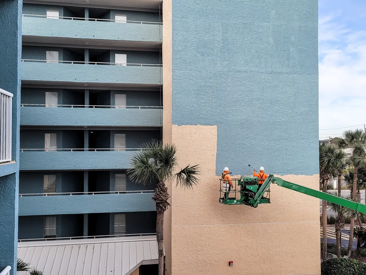Painters on a boom lift coating the exterior of a commercial building