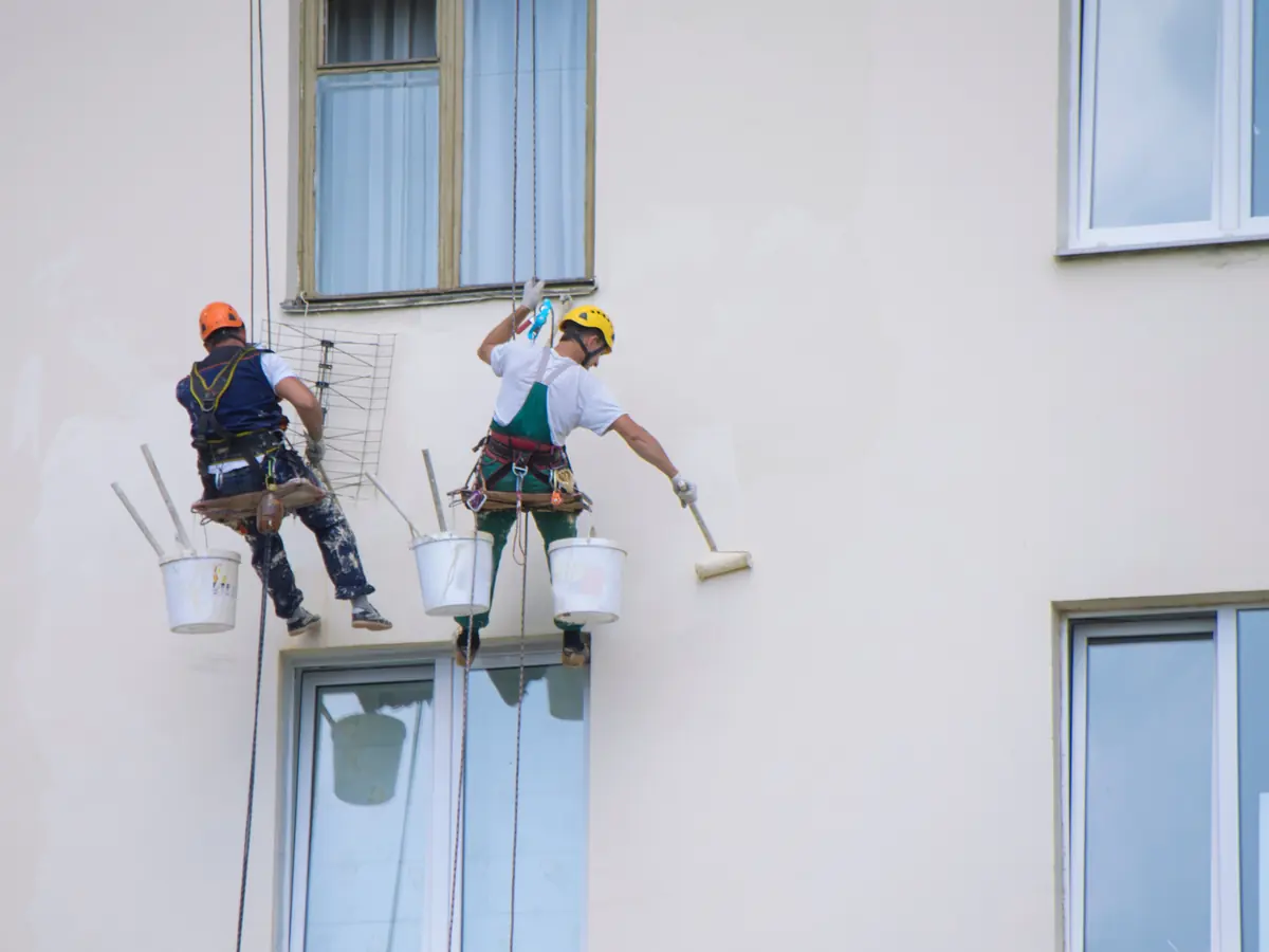 Two painters on ropes rolling fresh paint onto a building exterior