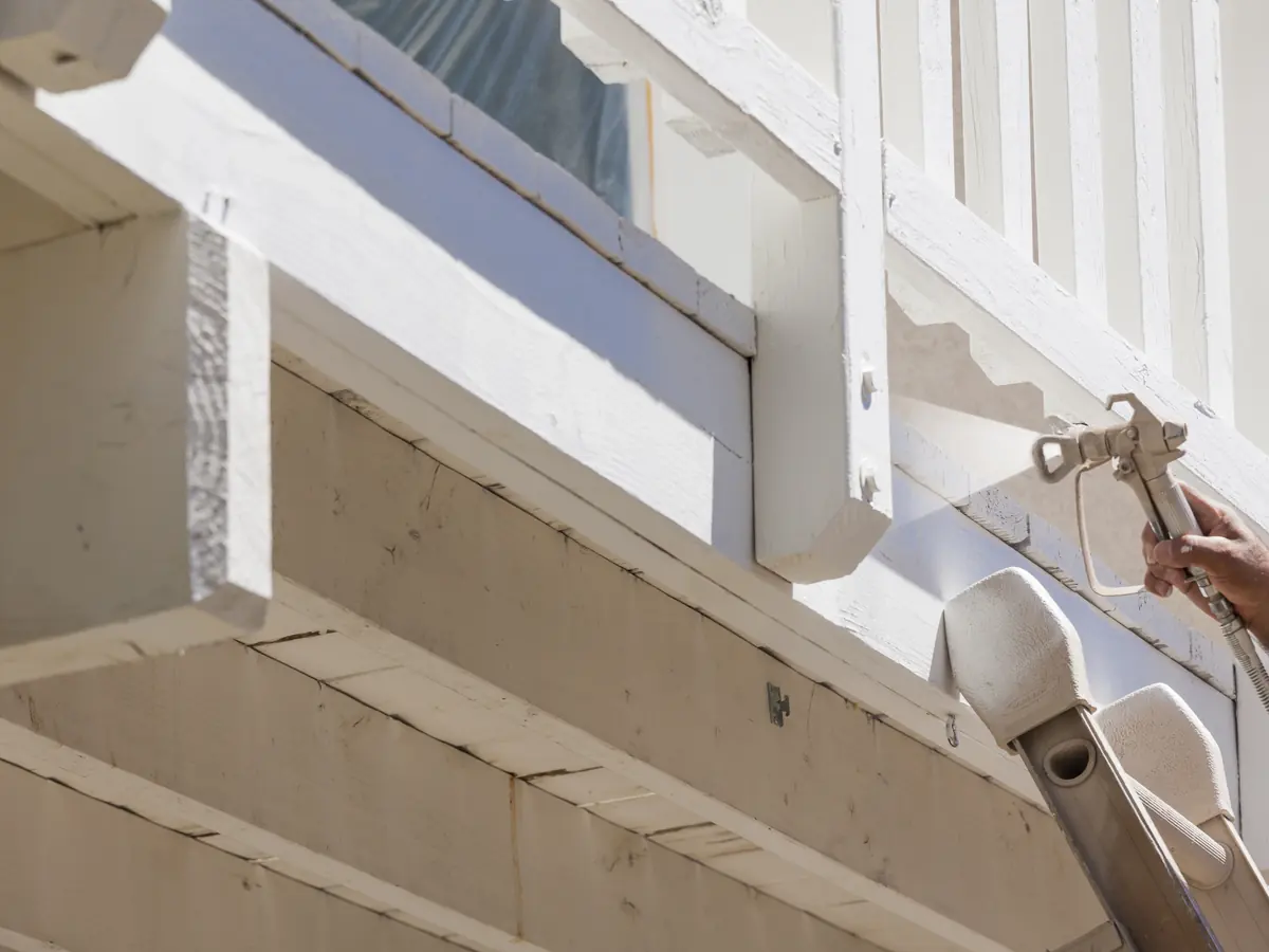 Painter in a respirator spraying exterior trim and railing white