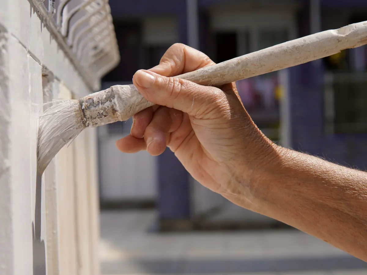 Hand brushing white paint onto exterior trim in daylight