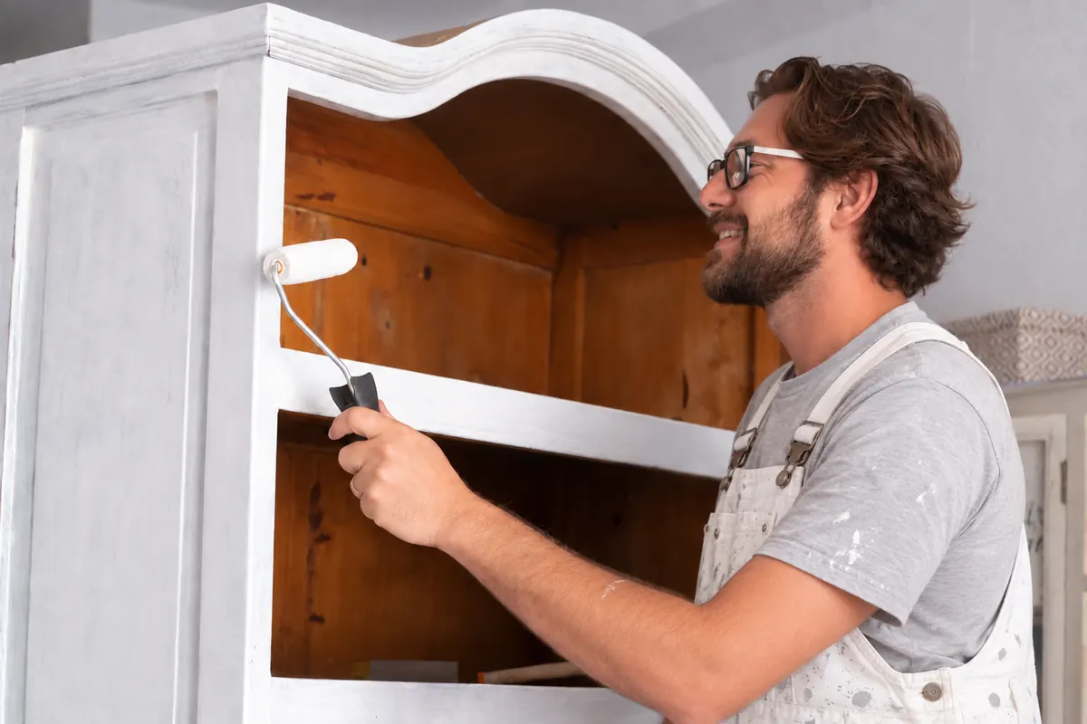 Painter rolling white paint onto a wooden armoire, furniture painting by Blue Oak Painting Company in Houston, TX