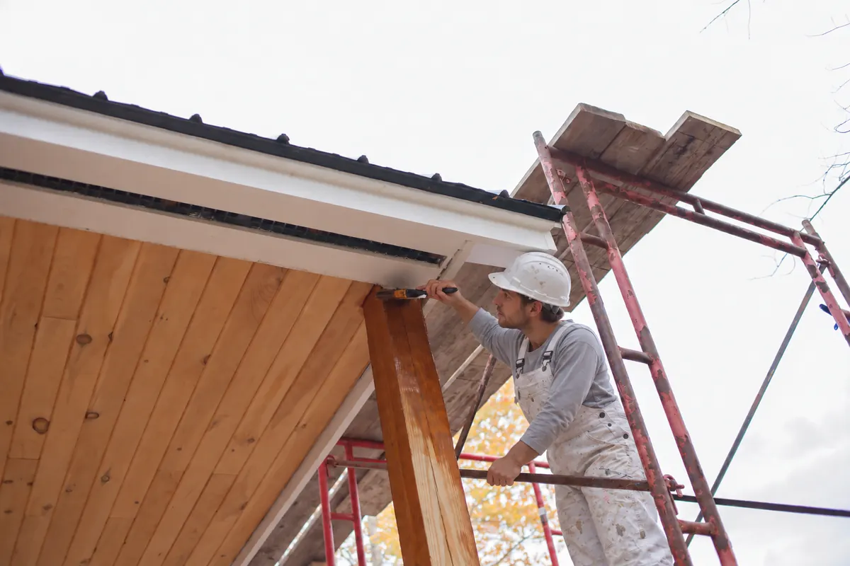 Painter on scaffolding brushing paint onto roofline trim and gutter fascia, gutter painting by Blue Oak Painting Company in Houston, TX