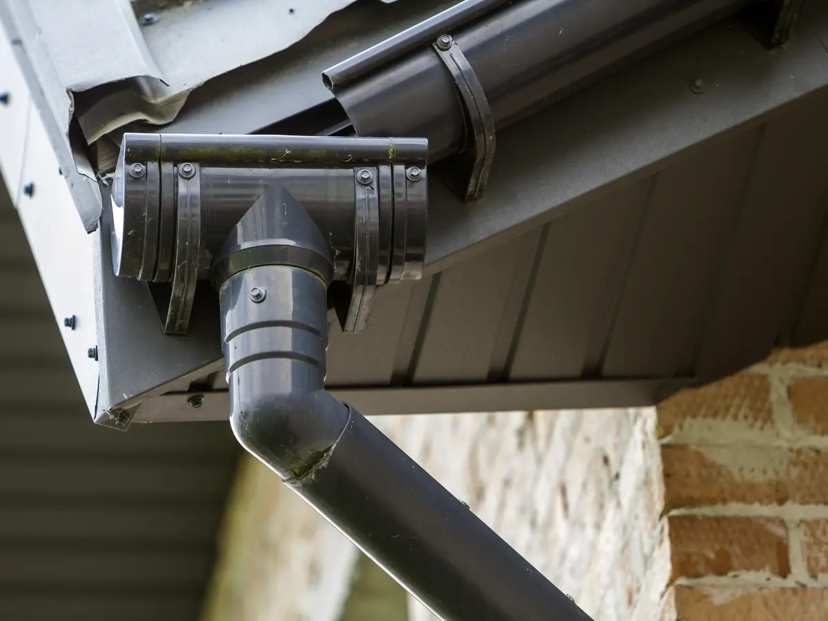 Dark gray gutter and downspout against a brick wall