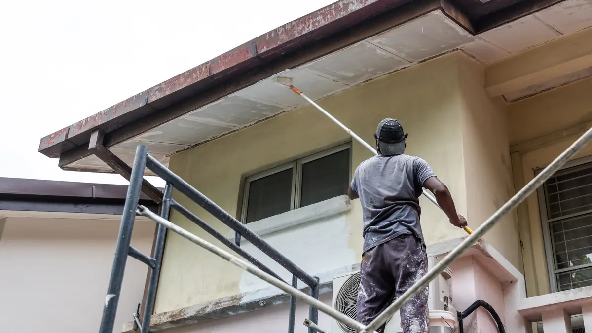 Painter on scaffolding rolling fresh paint onto the upper wall of a Houston area home