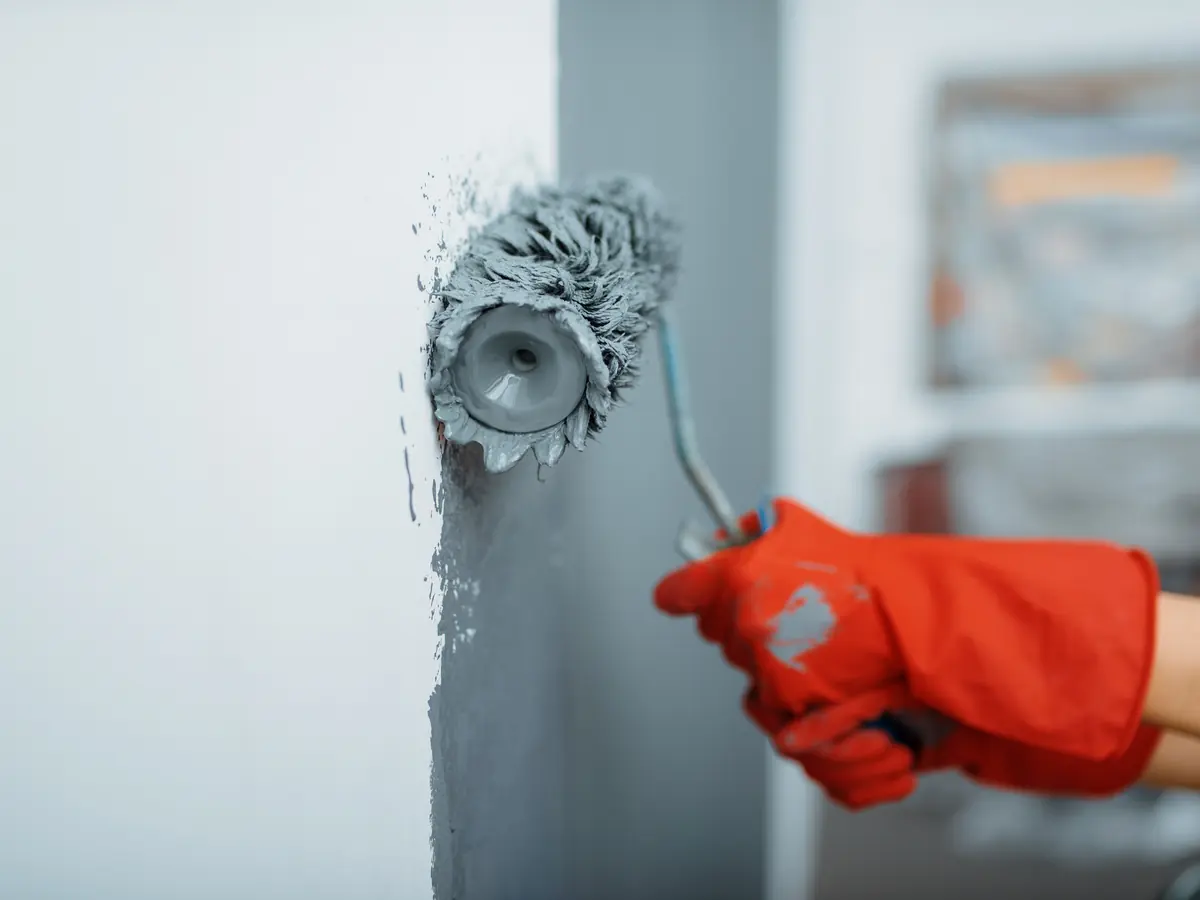 Roller applying a coat of gray paint to an interior wall