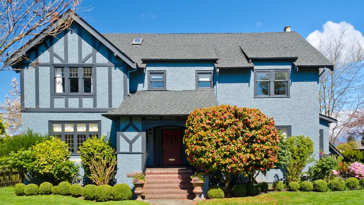 Two-story Tudor style home with blue gray siding, white trim and a landscaped front yard in a Katy, TX neighborhood