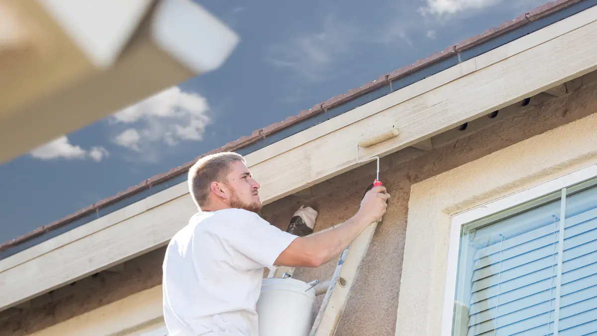 Painter on a ladder brushing the fascia and eaves of a stucco home in Spring, TX