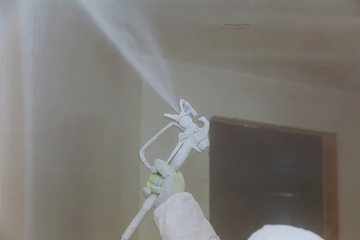 Painter in protective gear spraying an interior wall white with an airless sprayer