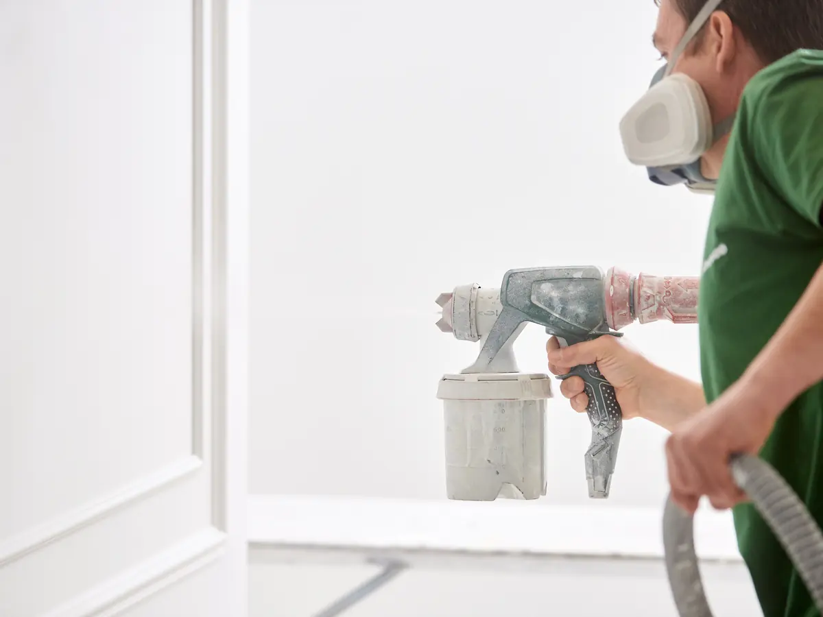 Painter in a respirator spraying an interior wall with an airless gun