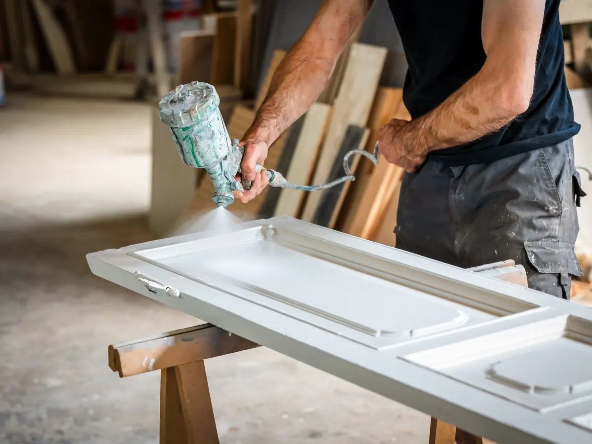 Craftsman spraying a paneled door white on sawhorses