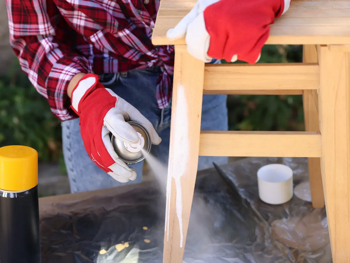 Spray can finishing a wooden stool white outdoors