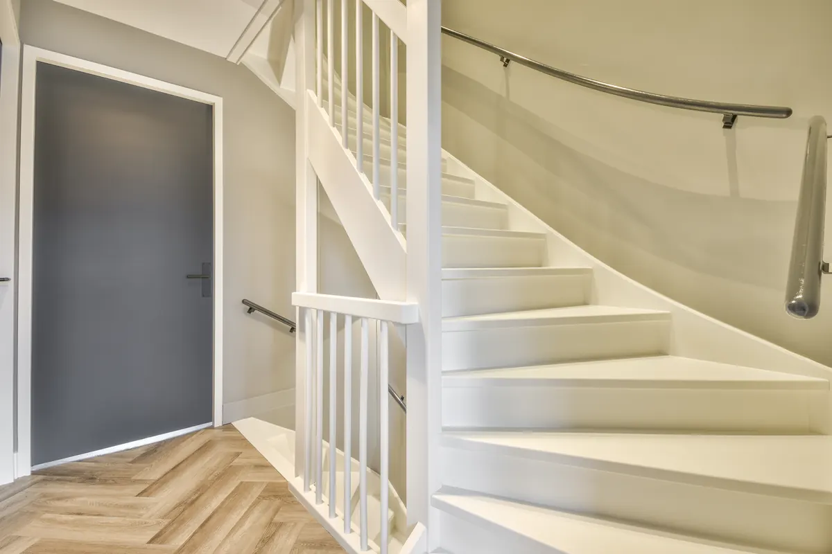 White painted staircase with spindles, treads and risers beside a gray door, staircase painting by Blue Oak Painting Company in Houston, TX