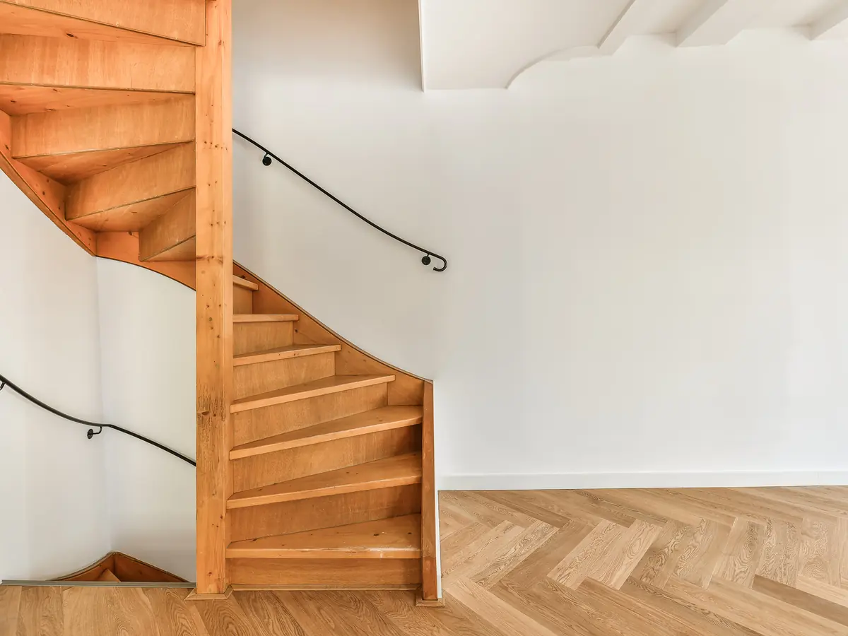 Wood staircase with a black handrail against white painted walls