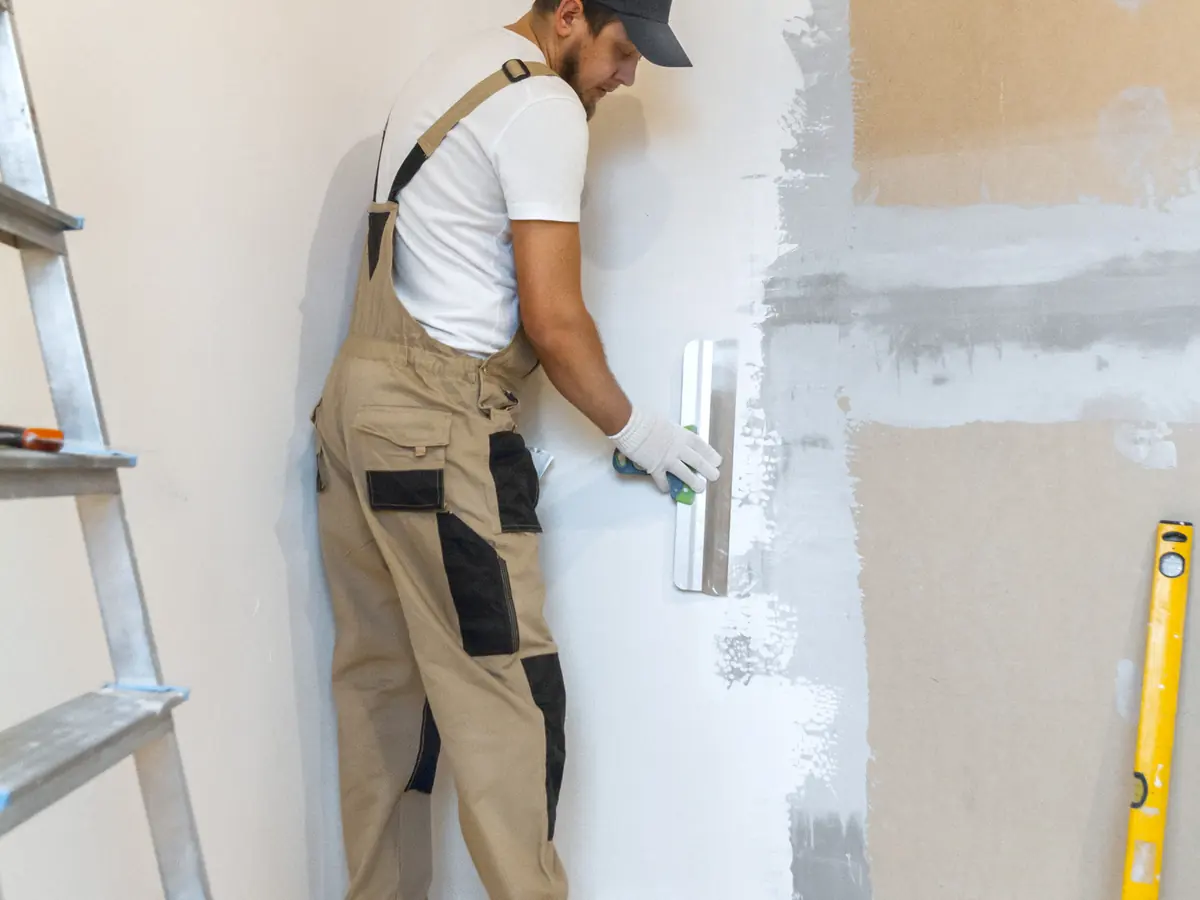 Painter skim coating a wall with a trowel after wallpaper removal